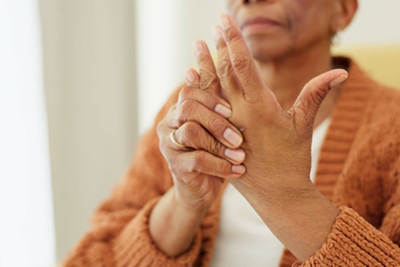An elderly woman holding her painful hand due to arthritis, illustrating joint stiffness and inflammation common in aging adults